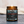 A lit amber glass jar candle with a black and red label reading 'ALMOST BIRTHDAY GIRL' by Last Looks Grooming Co, set on a gray textured surface with a soft beige background.