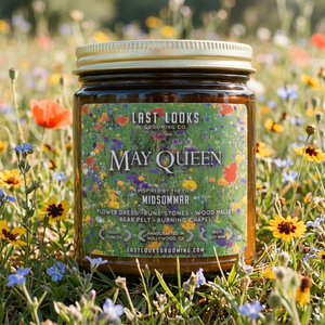 A jar of Last Looks Grooming Co. 'May Queen' movie candle sits in a field of colorful wildflowers.