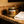 A Saltburn candle in a dark amber glass jar with a gold lid sits on a brown marble countertop next to a folded white towel. The label reads 'Last Looks Candle Co.